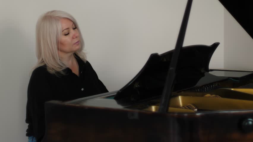 beautiful caucasian woman blonde 45-50 years old plays the piano, concept learning to play the piano, music lessons