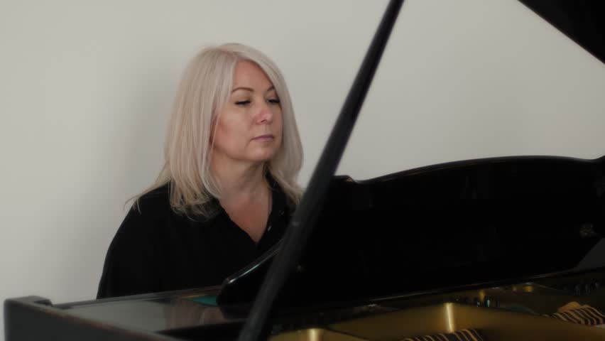 beautiful caucasian woman blonde 45-50 years old plays the piano, concept learning to play the piano, music lessons