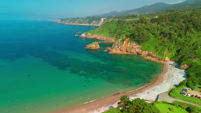 Aerial view of a beautiful Playa de Cadavedo beach surrounded by stunning nature of Asturias in northern Spain. White sand beach with turquoise sea water and steep cliffs of the Cantabrian Sea coast.