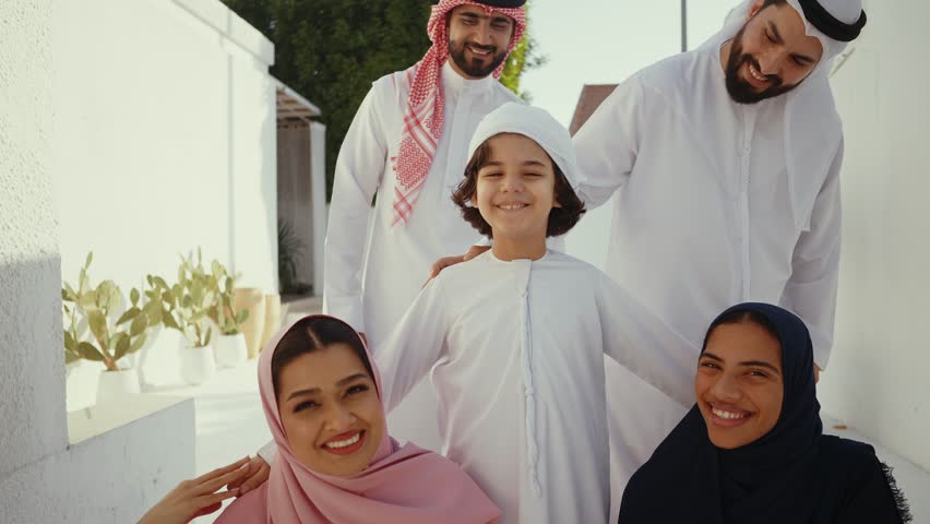 Arab family members wearing traditional attire standing together, sharing genuine moments of happiness, connection, and cultural pride in warm, intimate family portrait setting