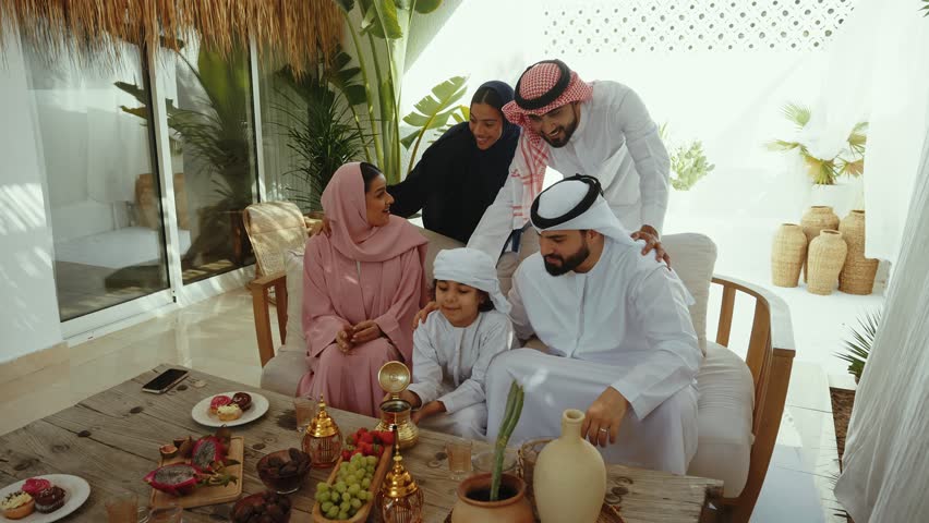 Emirati family wearing traditional clothing enjoying conversation and sharing diverse fruits and tea around wooden table in warm home interior