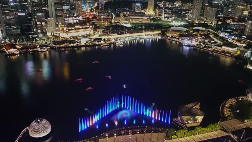 Marina Bay dancing fountain lights show at night in front of Singapore skyline. Aerial drone 4K video footage 