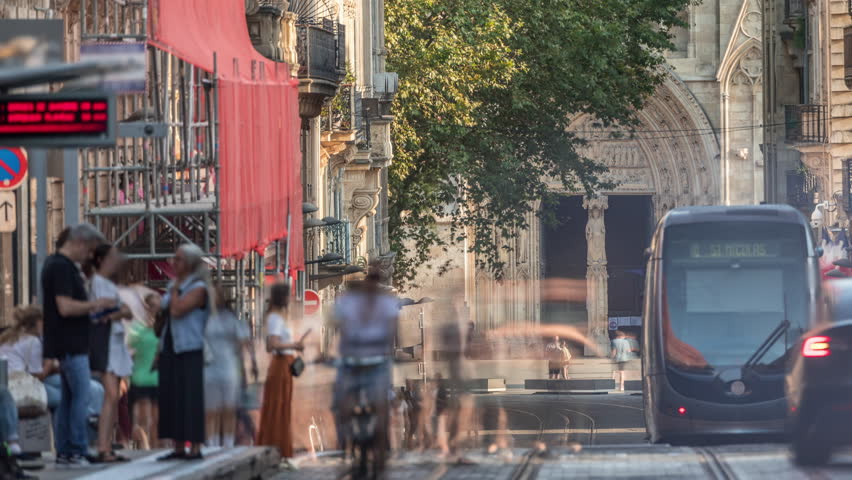 Timelapse of Bordeaux Cathedral entrance (Cathedrale Saint Andre) from Vital Carles street, featuring a moving tram in the historic city. People wait at the tram stop. A symbol of heritage. France
