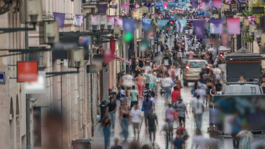 Tourists and locals walking and shopping in Rue Sainte-Catherine timelapse, Bordeaux, France. The longest pedestrian street in the country. Atmosphere of urban life. Colorful flags decorate the street