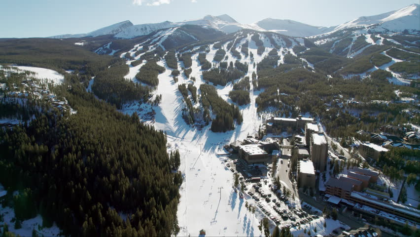An aerial view of the popular Breckenridge ski resort in Colorado, with snow covered mountain peaks and high altitude trails full of winter skiers and snowboarders on a sunny winter day.