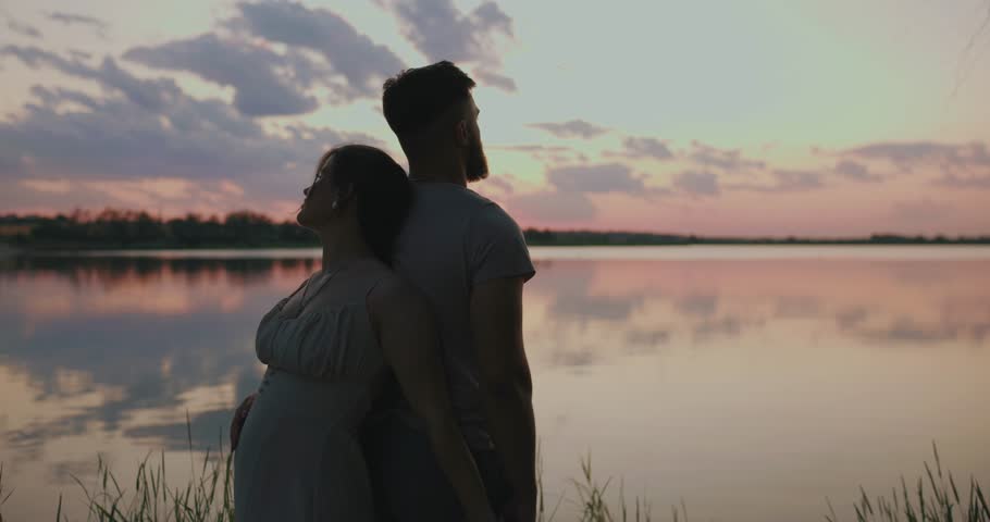 Silhouette of young couple standing near the lake waiting for a baby