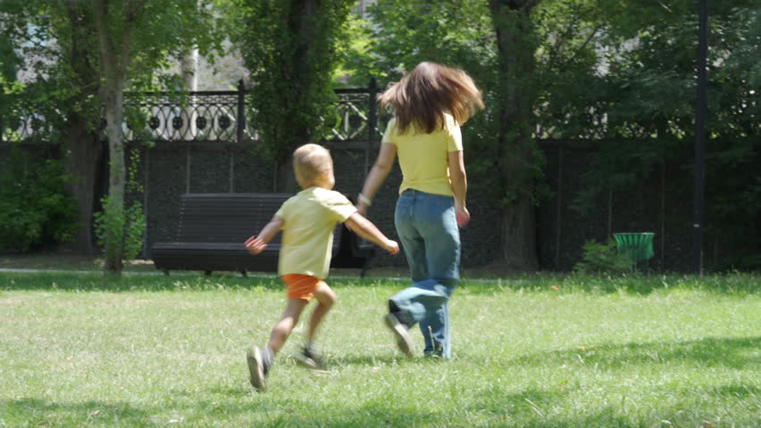 A woman and a young boy are playing frisbee in a green park in Simferopol, Crimea. They enjoy a bright, sunny day surrounded by trees and open grass.