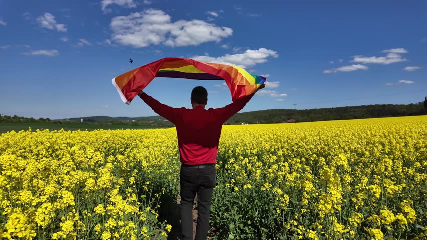 LGBTQ+ visibility: Man with rainbow flag amidst flowering fields.