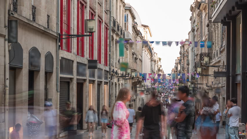 Tourists and locals walking and shopping in Rue Sainte-Catherine timelapse, Bordeaux, France. The longest pedestrian street in the country. Colorful flags decorate the street. Atmosphere of urban life