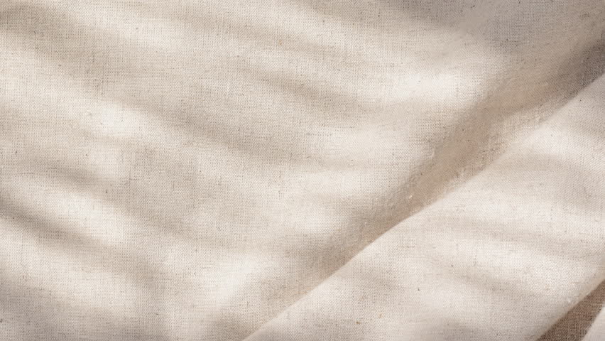 Camera pushes into folded linen weave as sunlight reveals warm tactile detail