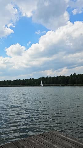 Sailing on a serene lake surrounded by lush trees under a partly cloudy sky