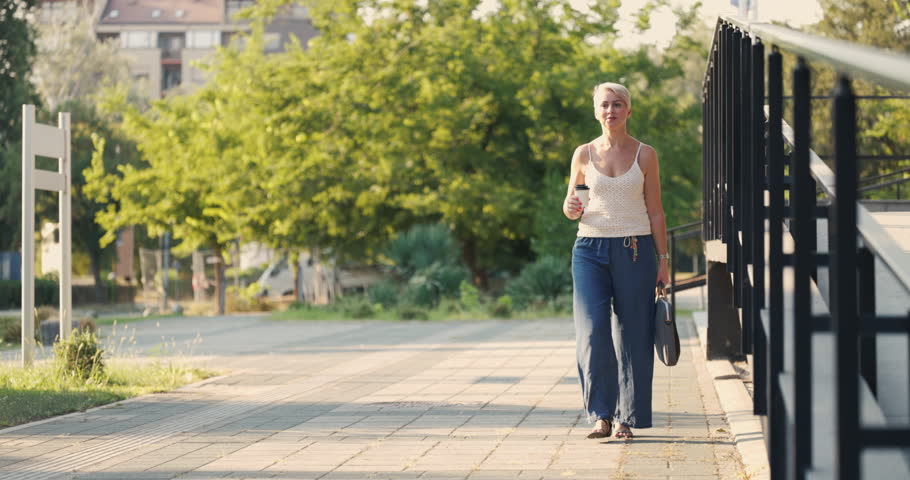 Happy middle age woman walking outside with her coffee to go.