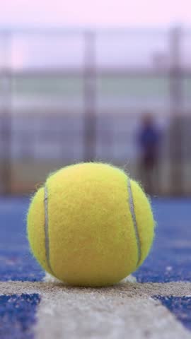 Yellow ball on floor behind padel net in blue court outdoors. Man who playing paddle tennis. One caucasian player sportman hitting balls. Racquet sport game Concept.