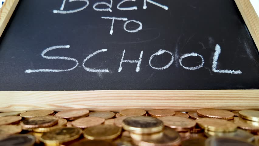 Euro coins scattered on a table with a small blackboard with the words back to school written on it and colored pencils and adhesive tape in the background