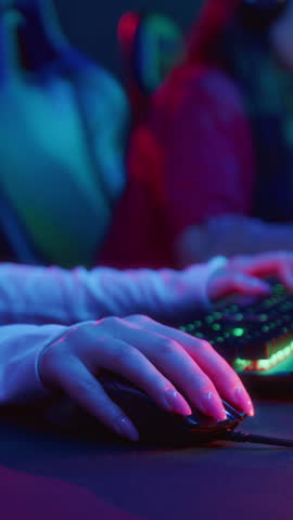 Vertical closeup of hands of anonymous young female gamer, with natural manicure, playing shooter in cyberclub, using mouse and computer keyboard