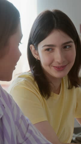 Vertical shot of two young women studying together and chatting while eating snacks in dorm room