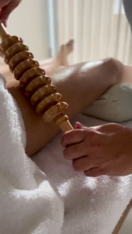 Young woman receiving a massage from a professional masseuse at a spa salon, lying on a massage table, with lotions and wooden traditional tools
