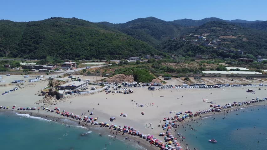 Aerial view of a summer vacation beach crowded with people swimming and having fun enjoying the holiday, a sandy beach full of umbrellas on a hot day and an island in Mediterranean sea, jijel Algeria.