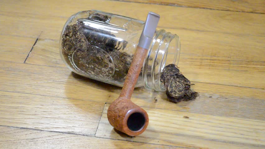 Video of brown tobacco pipe leaning against glass jar filled with tobacco. 