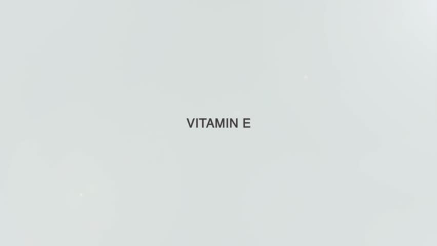 A hand holds a magnifying glass over the words "Vitamin E" on a white background. The lens enlarges the phrase, symbolizing focus on antioxidant protection, skin health, and the essential role of this