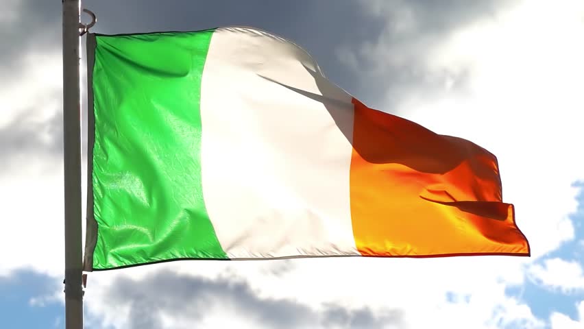 The national flag of Ireland, vibrant green, white, and orange, waves proudly against a dramatic, cloudy sky, symbolizing national identity.