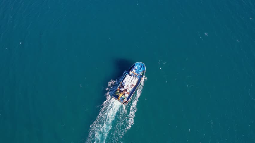Inland cargo ship in blue sea water or river, aerial top view. Service auxiliary boat for fishing nets and fish farms trout cages.