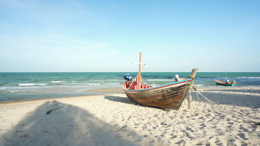 two traditional fishing boats or small old wooden tourist boat anchored parked on sand beach with little wave of sea in ocean marine at Hua Hin in Thailand on daylight sky for summer holiday travel