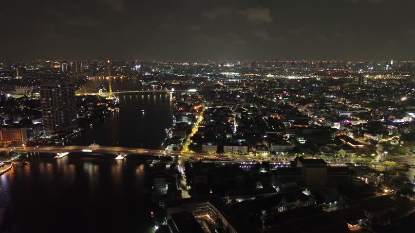 Aerial view of illuminated Rama VIII Bridge at night. Cable-stayed bridge crossing Chao Phraya River in Bangkok, Thailand, 4k