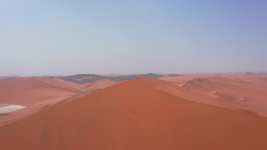 Aerial footage of tourists standing atop Big Daddy dune in Sossusvlei, Namibia, surrounded by sweeping desert landscapes and vast orange sand