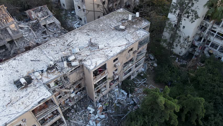 Drone shot over damaged buildings in Tel Aviv. Rubble and collapsed trees are visible after Iranian missile strikes.