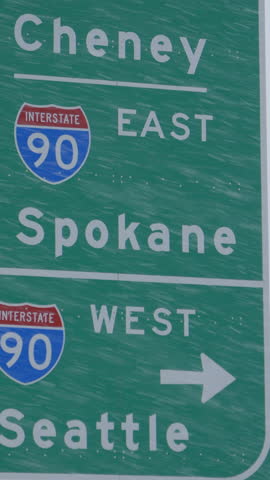 CLOSE UP: Traffic sign weathers a severe blizzard engulfing the state of Washington. Green highway traffic sign directs traffic around the state of Washington during a snowstorm. Extreme weather.