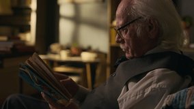 Side view shot of focused elderly Caucasian man in retro eyeglasses reading book sitting in armchair in his cozy study room - Powered by Shutterstock - Get 15% off with code: PIKWIZARD15