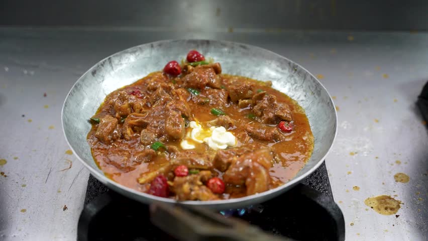 Close-up of a chef stirring spicy chicken karahi in a wok over open flame at street kitchen. Pakistan