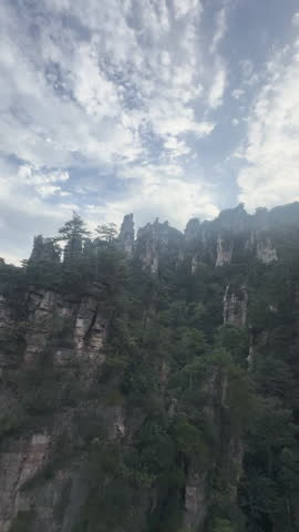 Tall sandstone cliffs with tree cover rise through misty mountain landscape in Zhangjiajie National Forest Park , tc01