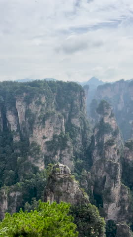 Tall sandstone cliffs with tree cover rise through misty mountain landscape in Zhangjiajie National Forest Park , tc01