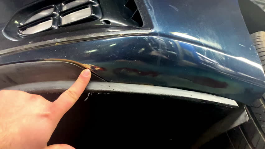 Man looking examining scratch on his car bamper.Unexpectable vehicle damage trouble accident.Road safety and automobile insurance,garage workshop,auto service
