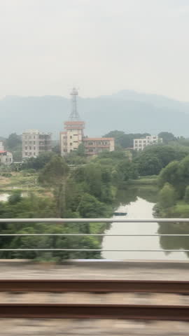 Train view of tracks, green fields, river, and misty hills in Guangxi under cloudy sky, tc01
