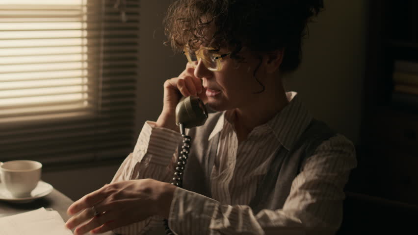 Zoom out shot of middle-aged Caucasian female author talking on retro rotary phone discussing deadline of her new book with publisher sitting at desk in front of vintage typewriter