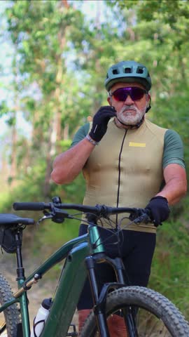 vertical Seasoned senior cyclist confidently adjusting sport helmet while wearing sunglasses during forest e-bike expedition, embodying active retirement lifestyle and outdoor adventure