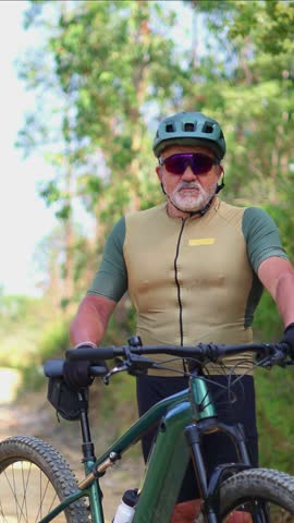 vertical Seasoned senior cyclist confidently adjusting sport helmet while wearing sunglasses during forest e-bike expedition, embodying active retirement lifestyle and outdoor adventure