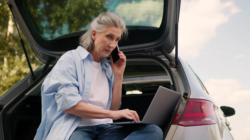 Angry shouting Caucasian elderly business woman car driver mad businesswoman female freelancer annoyed boss talking yelling mobile phone quarrel conflict work trouble typing laptop device outside park