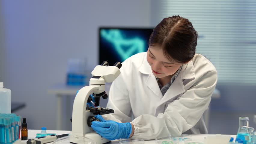 Professional female scientist in white coat and blue gloves using microscope in modern laboratory, conducting experiments and analyzing samples - Powered by Shutterstock - Get 15% off with code: PIKWIZARD15