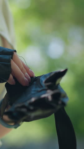 Close-up of individual outdoors fastening biker glove on left hand with focused gesture, background shows blurred trees and lush greenery