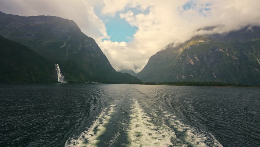 Scenic ferry cruising on Milford Sound surrounded by mountain, waterfall and misty fjord in Fiordland National Park, New Zealand
