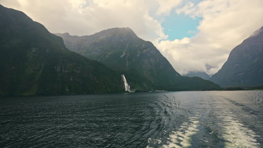Scenic ferry cruising on Milford Sound surrounded by mountain, waterfall and misty fjord in Fiordland National Park, New Zealand