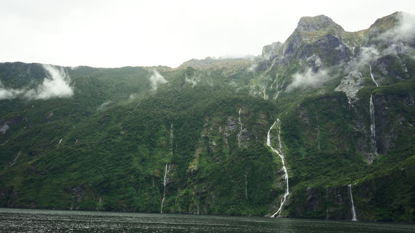 Scenic ferry cruising on Milford Sound surrounded by mountain, waterfall and misty fjord in Fiordland National Park, New Zealand