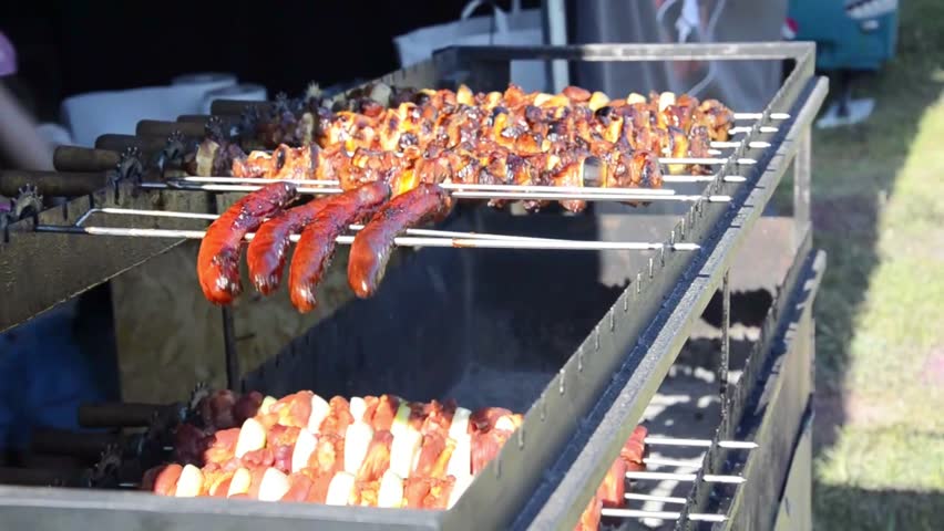 Meat on skewers and sausages are fried on the grill.Spinning barbecue for outdoor kitchen. Street restaurant.