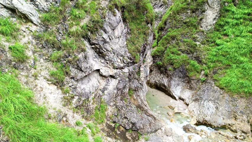 Exploring a hidden natural rock formation and stream in a lush green landscape near a mountain river