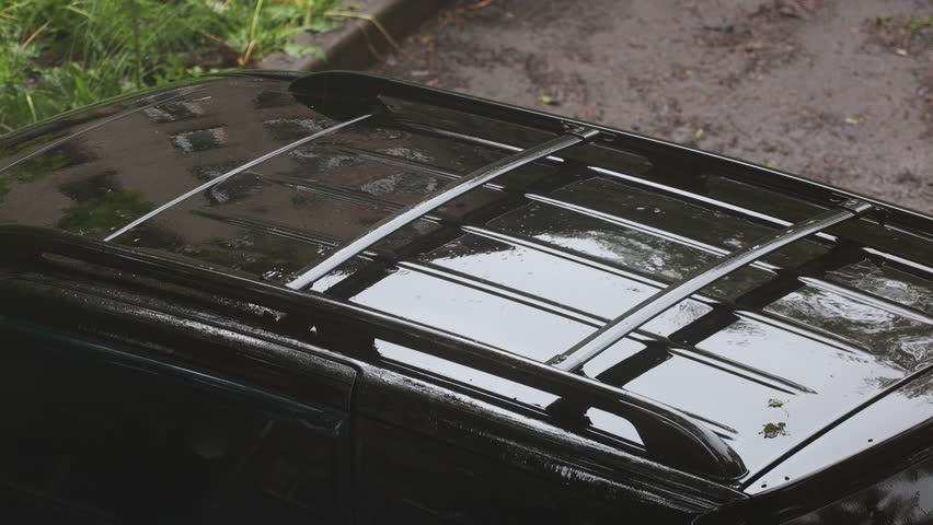 A black car is parked on the side of a road. Rainy weather