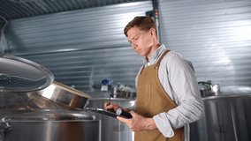 Brewer inspects fermentation tanks with tablet in modern brewery food factory. - Powered by Shutterstock - Get 15% off with code: PIKWIZARD15